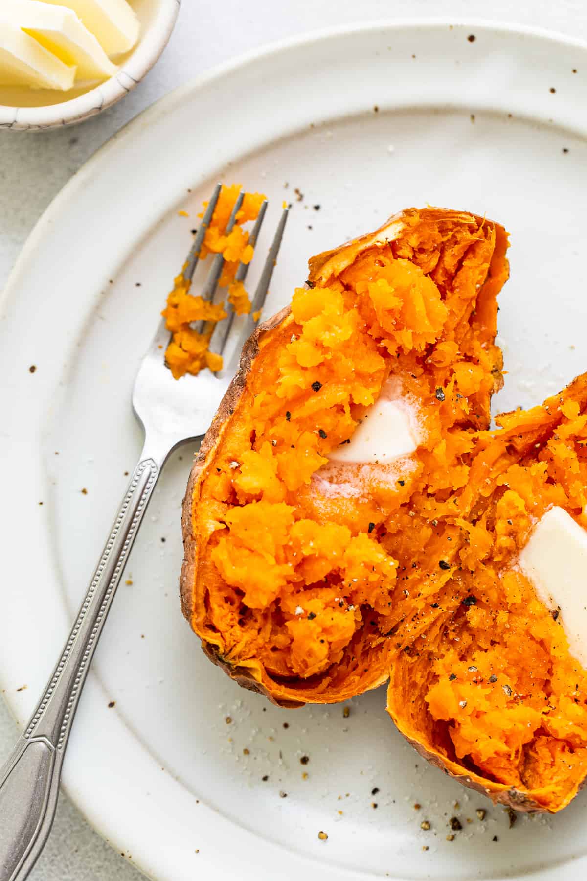 A cooked sweet potato on a plate with butter and pepper. 