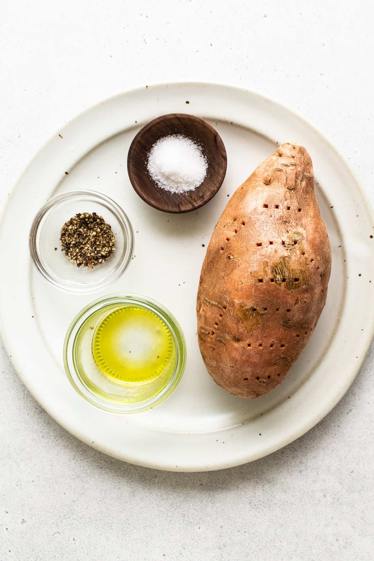 Una patata dolce, sale, pepe e olio su un piatto. 