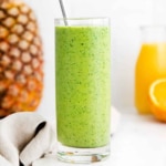 A green spinach smoothie in a glass with oranges and pineapples.
