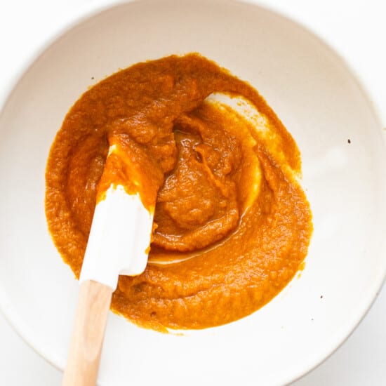 Pumpkin puree in a white bowl with a wooden spatula.