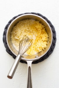 A pan with cheese in it and a whisk.