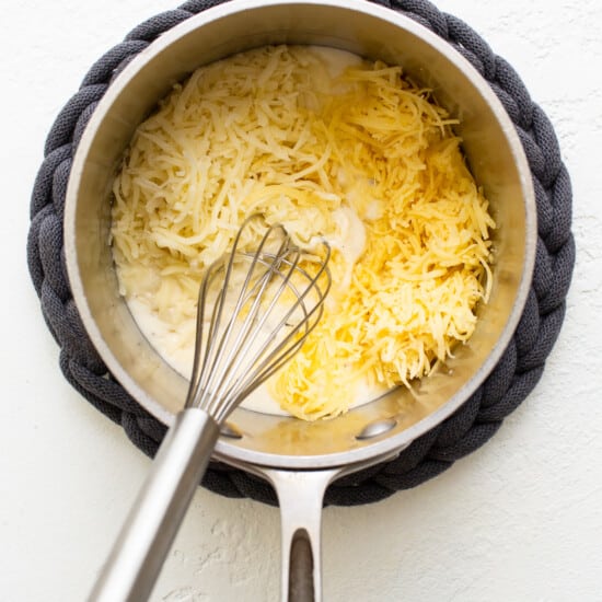 A pan with cheese in it and a whisk.