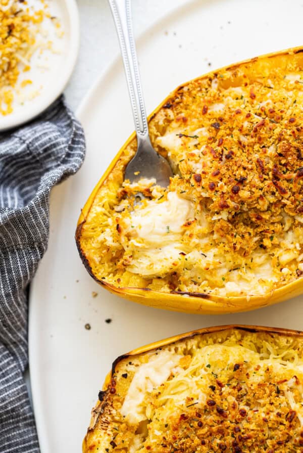 Two spaghetti squash boats filled with mac and cheese on a plate with a spoon.