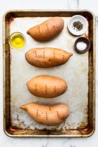Four sweet potatoes on a baking sheet with olive oil and spices.