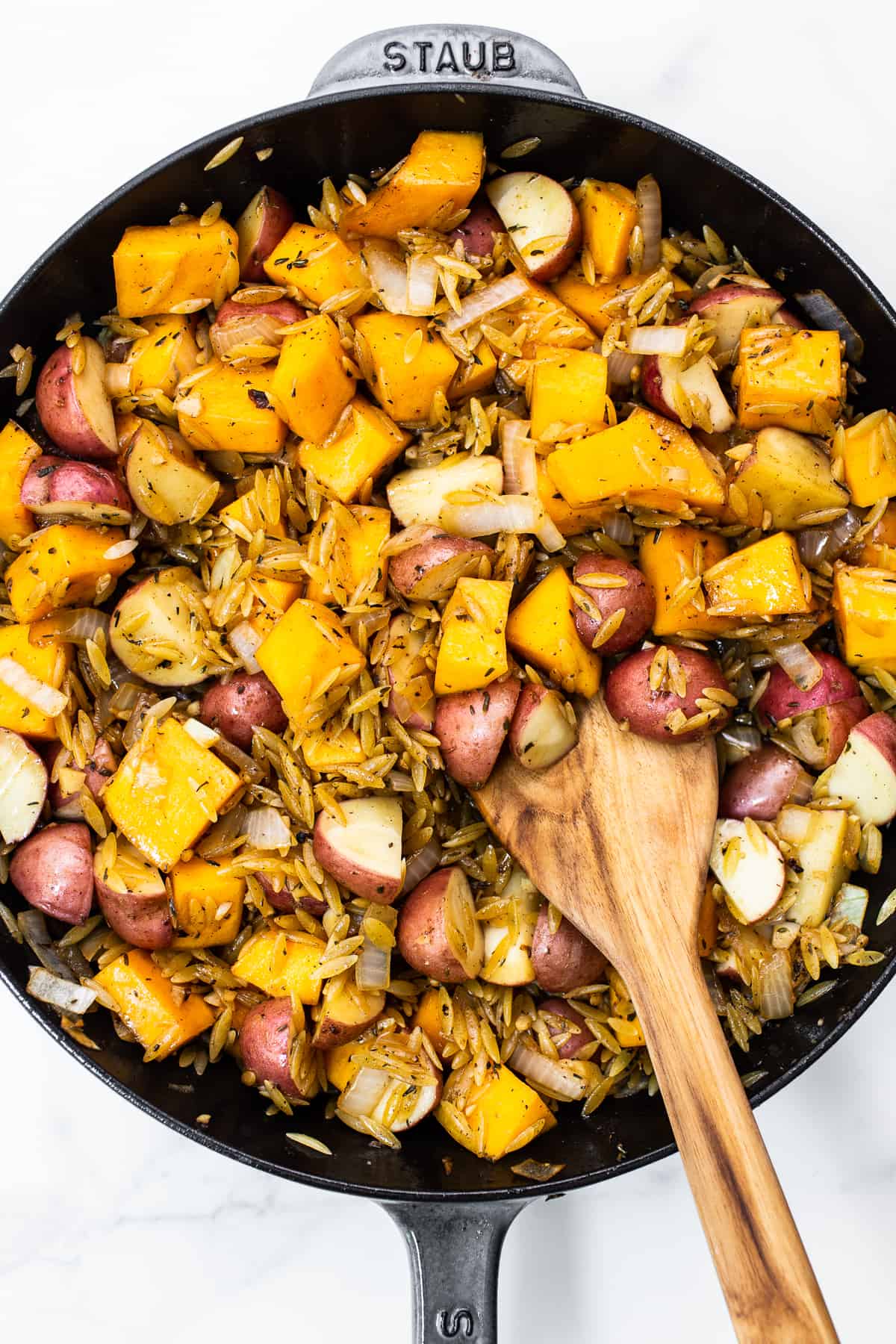 Orzo, butternut squash, and red potatoes in a cast iron skillet. 