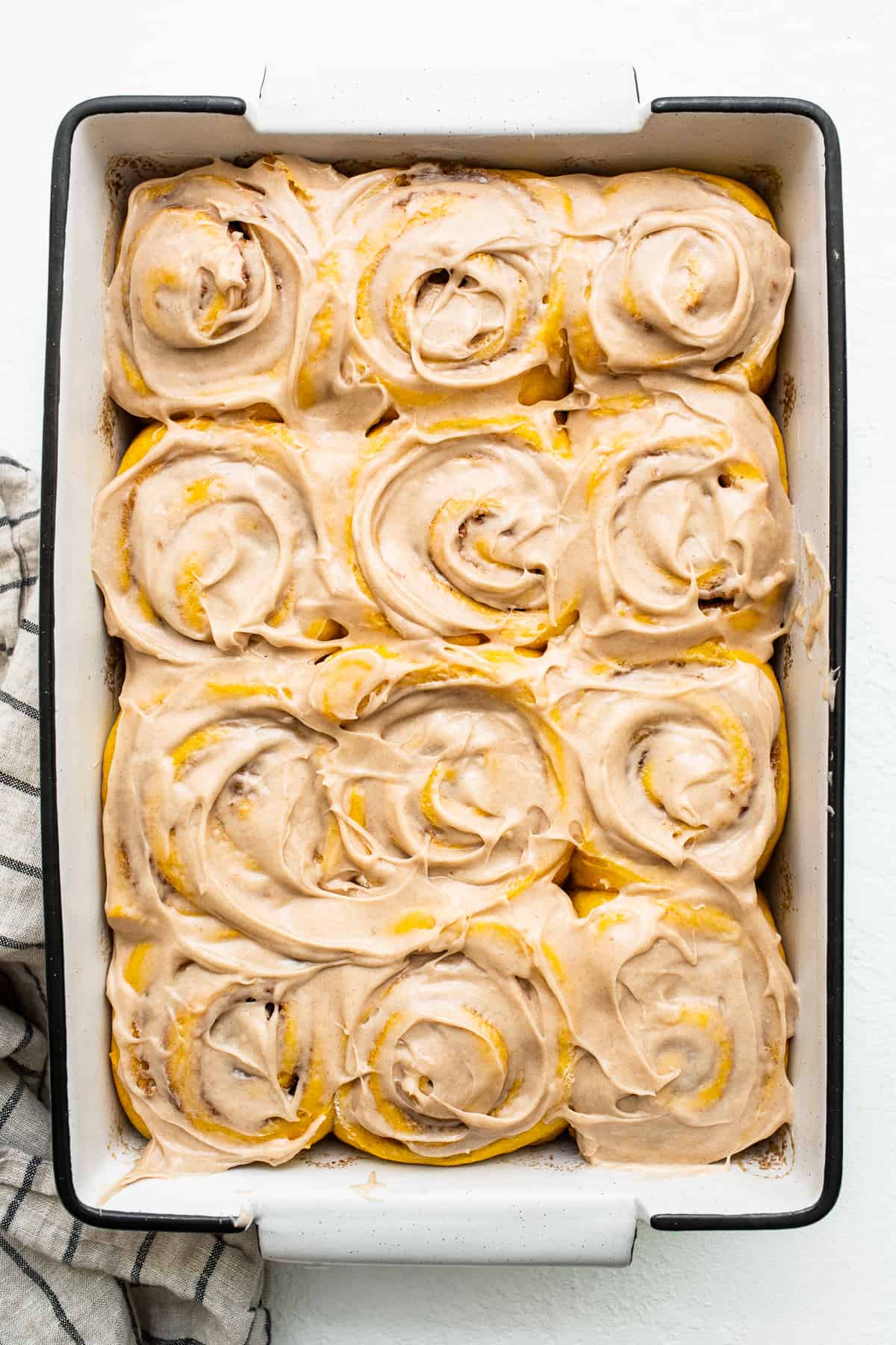 Pumpkin cinnamon rolls topped with a cinnamon cream cheese frosting in a baking dish.