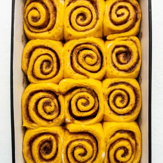 Cinnamon rolls in a baking dish on a white surface.