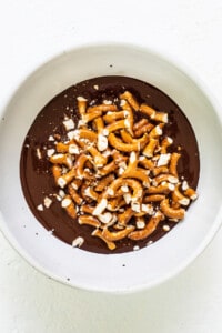 A white bowl filled with chocolate and pretzels.