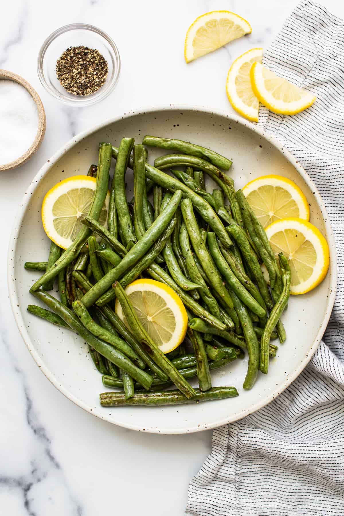 Green beans in a serving bowl with lemon slices. 