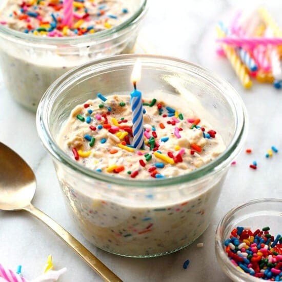 A birthday cake in a jar with a candle and sprinkles.