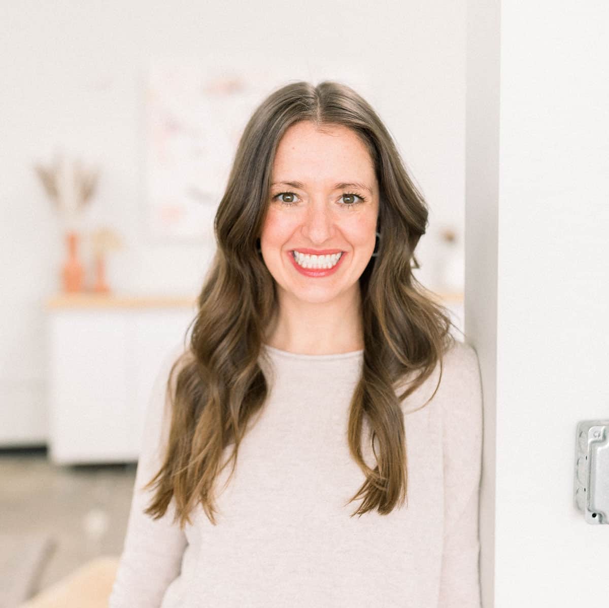 A fit foodie woman smiling in front of a wall.