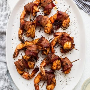Bacon wrapped shrimp skewers on a white plate.