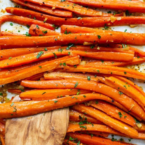 Carrots on a baking sheet with a wooden spoon.