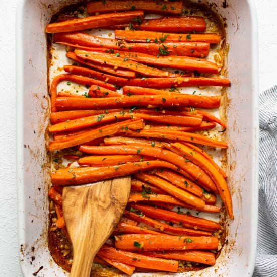 Roasted carrots in a baking dish with a wooden spoon.