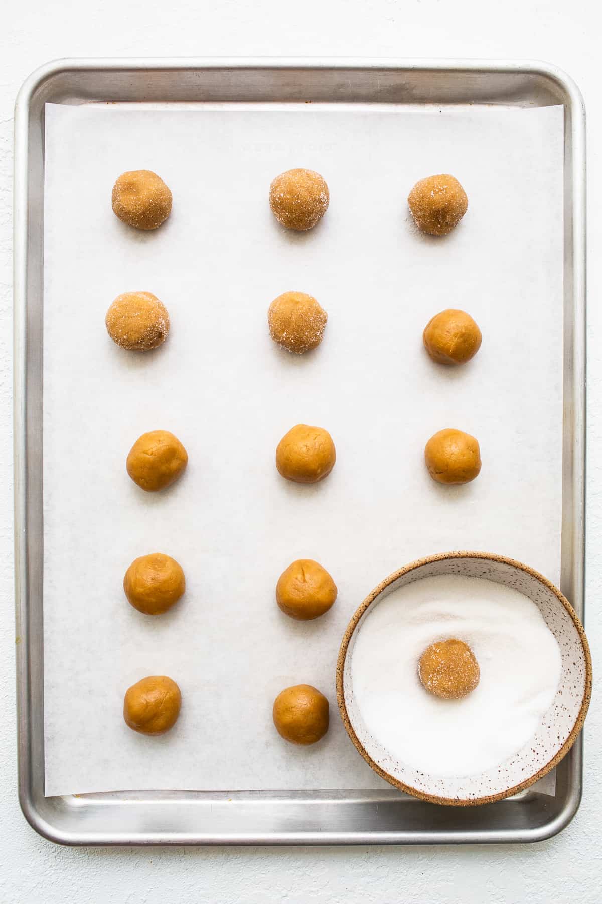 Peanut butter kiss cookie dough on a baking sheet rolled in sugar.