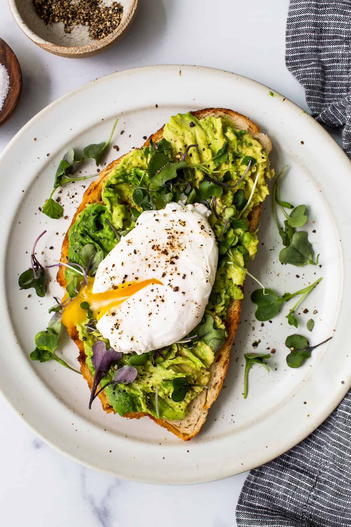 Poached egg on avocado toast on a plate with microgreens.