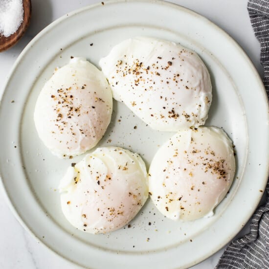 Four eggs on a plate with salt and pepper.