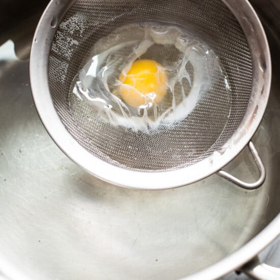 An egg is being fried in a metal strainer.