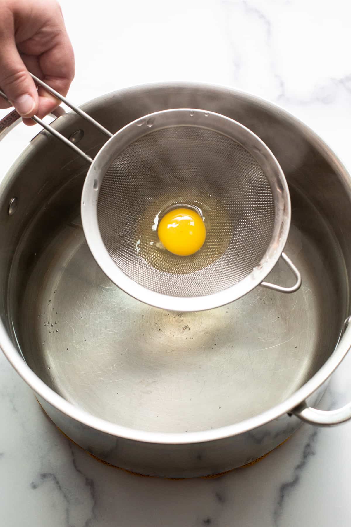 Raw egg in a strainer being set in a pot of boiling water.