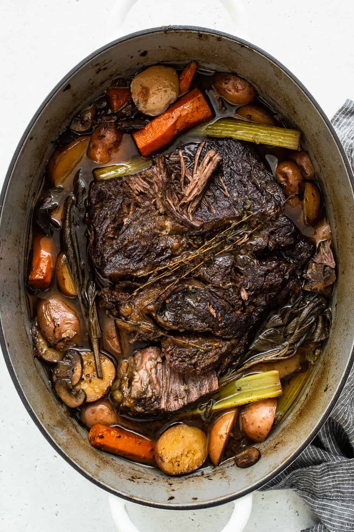 Cooked pot roast in a dutch oven surrounded by veggies.