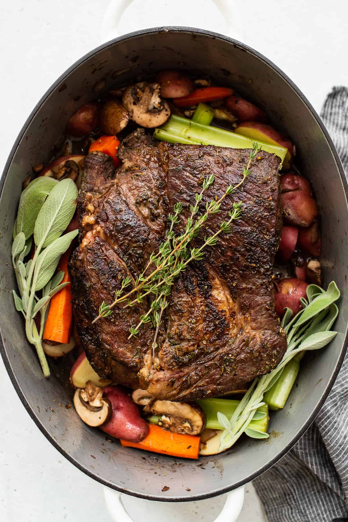 Pot roast in a dutch oven topped with fresh herbs.