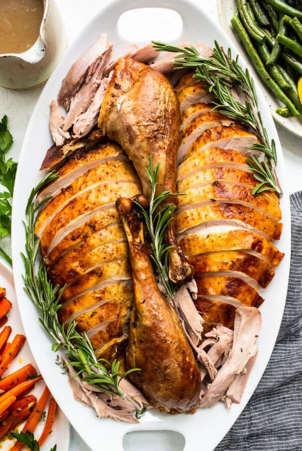 Roasted turkey with gravy and vegetables on a white platter.