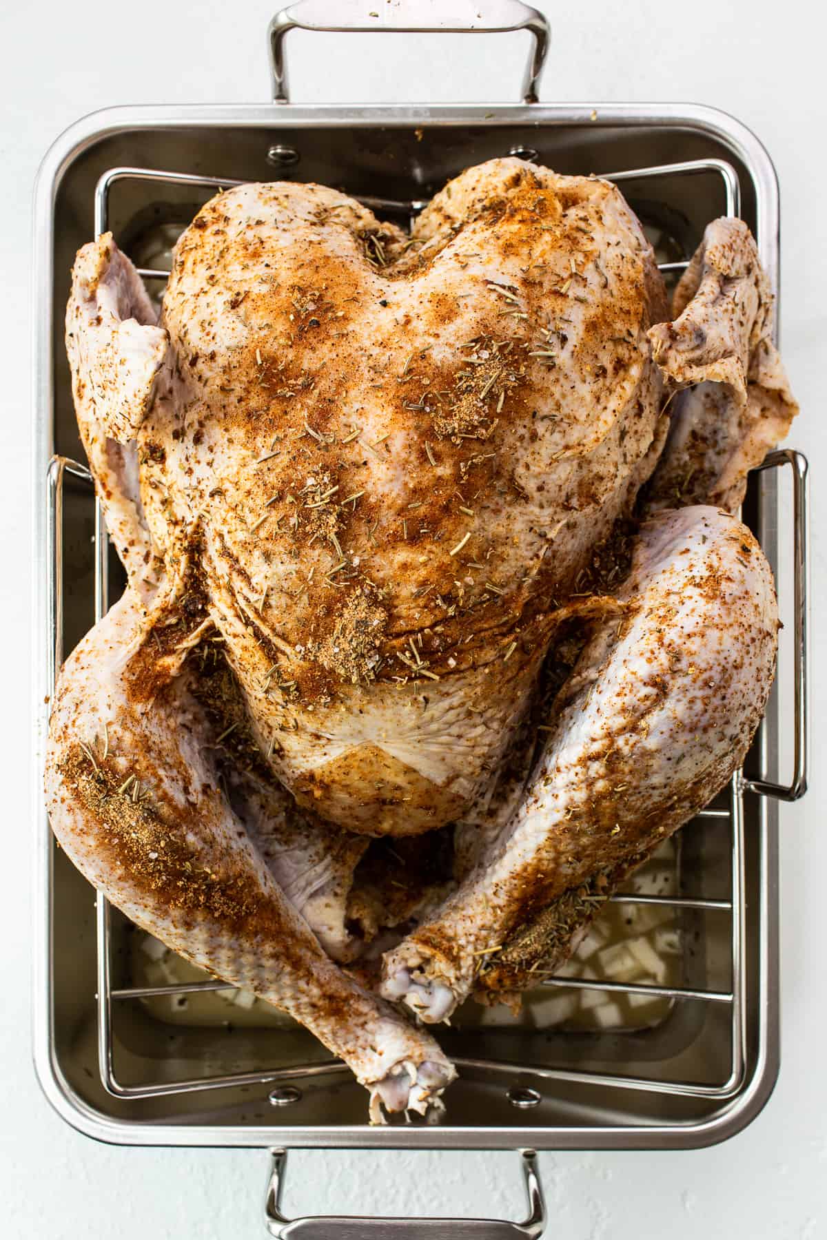 A whole turkey with dry rub and sitting in a roasting pan. 