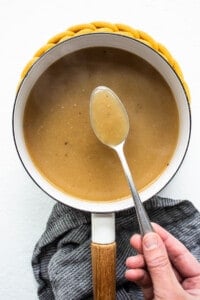 A person holding a spoon in a pot of gravy.