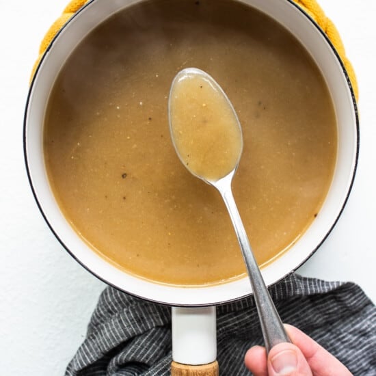 A person holding a spoon in a pot of gravy.
