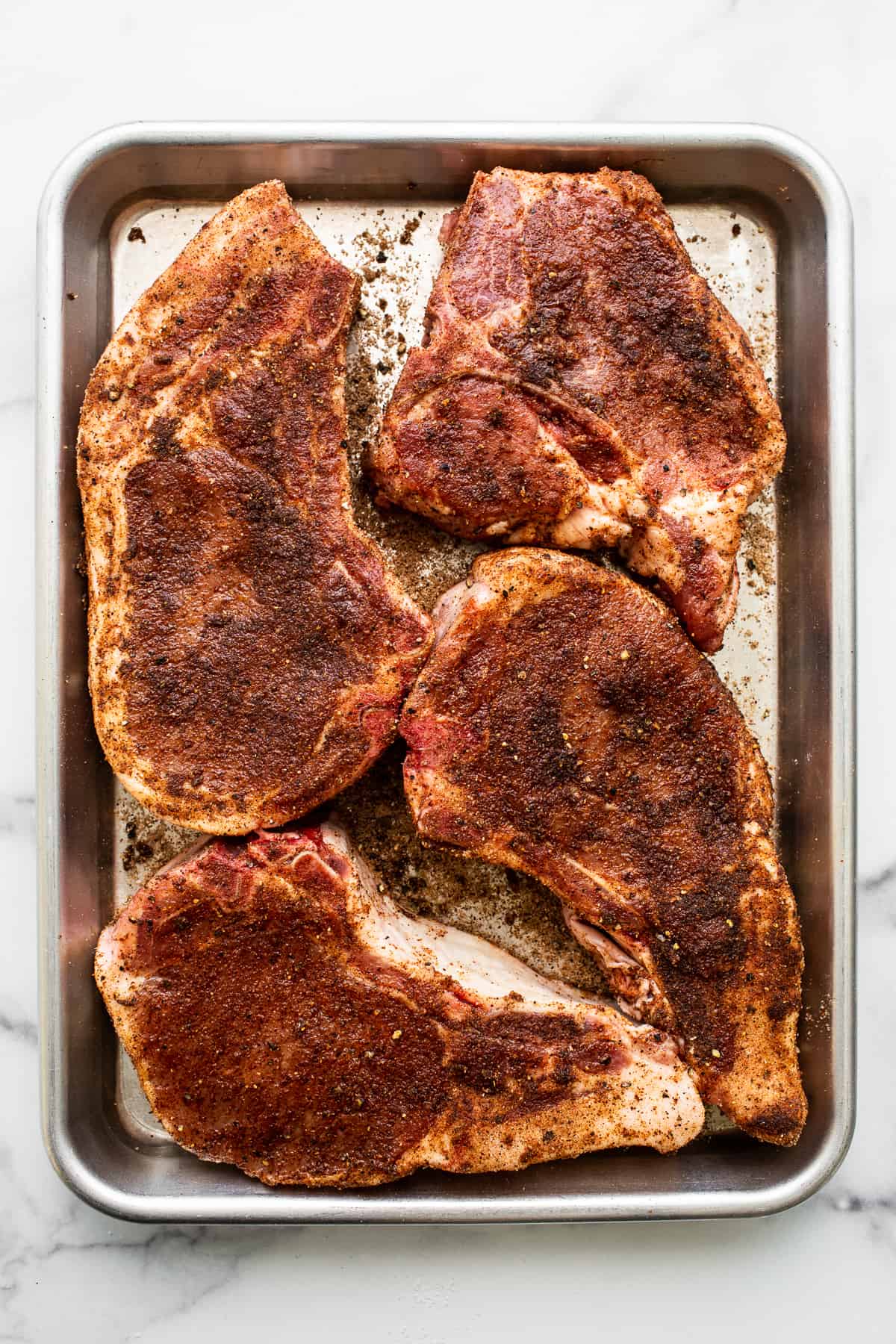 Raw pork chops on a baking sheet.