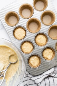 A muffin tin filled with muffin batter and a whisk.