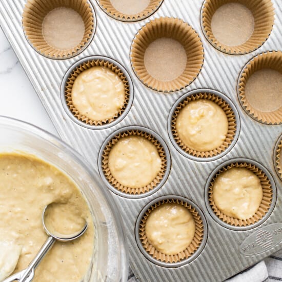 A muffin tin filled with muffin batter and a whisk.