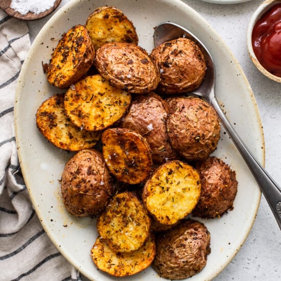 Roasted potatoes on a plate with ketchup and salt.