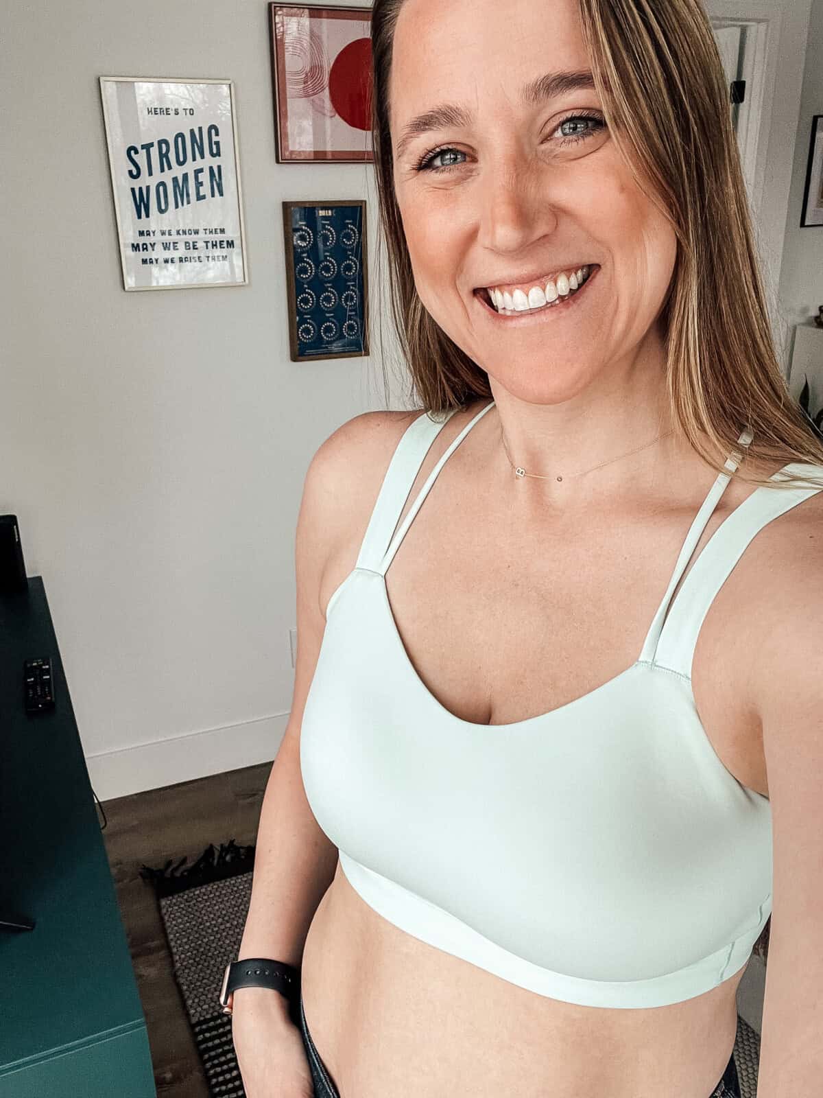 A smiling person wearing a light green lululemon bra takes a selfie in a room adorned with motivational posters.