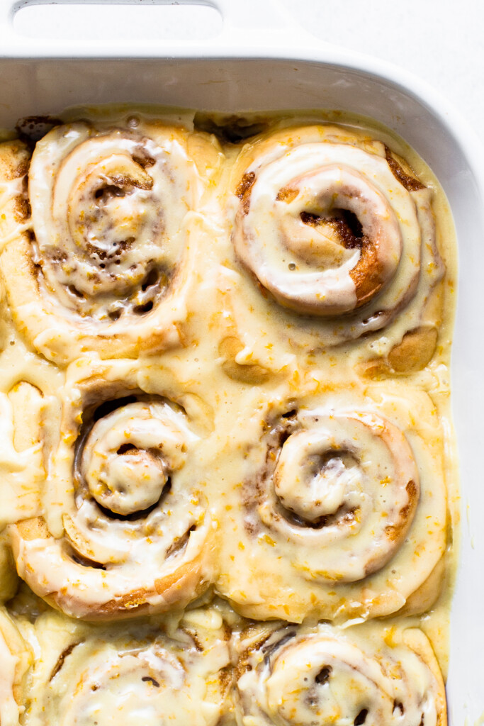 Frosted orange rolls in a casserole dish.