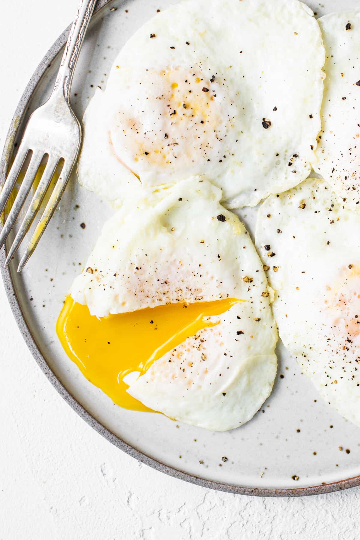 Over easy eggs on a plate with a fork.