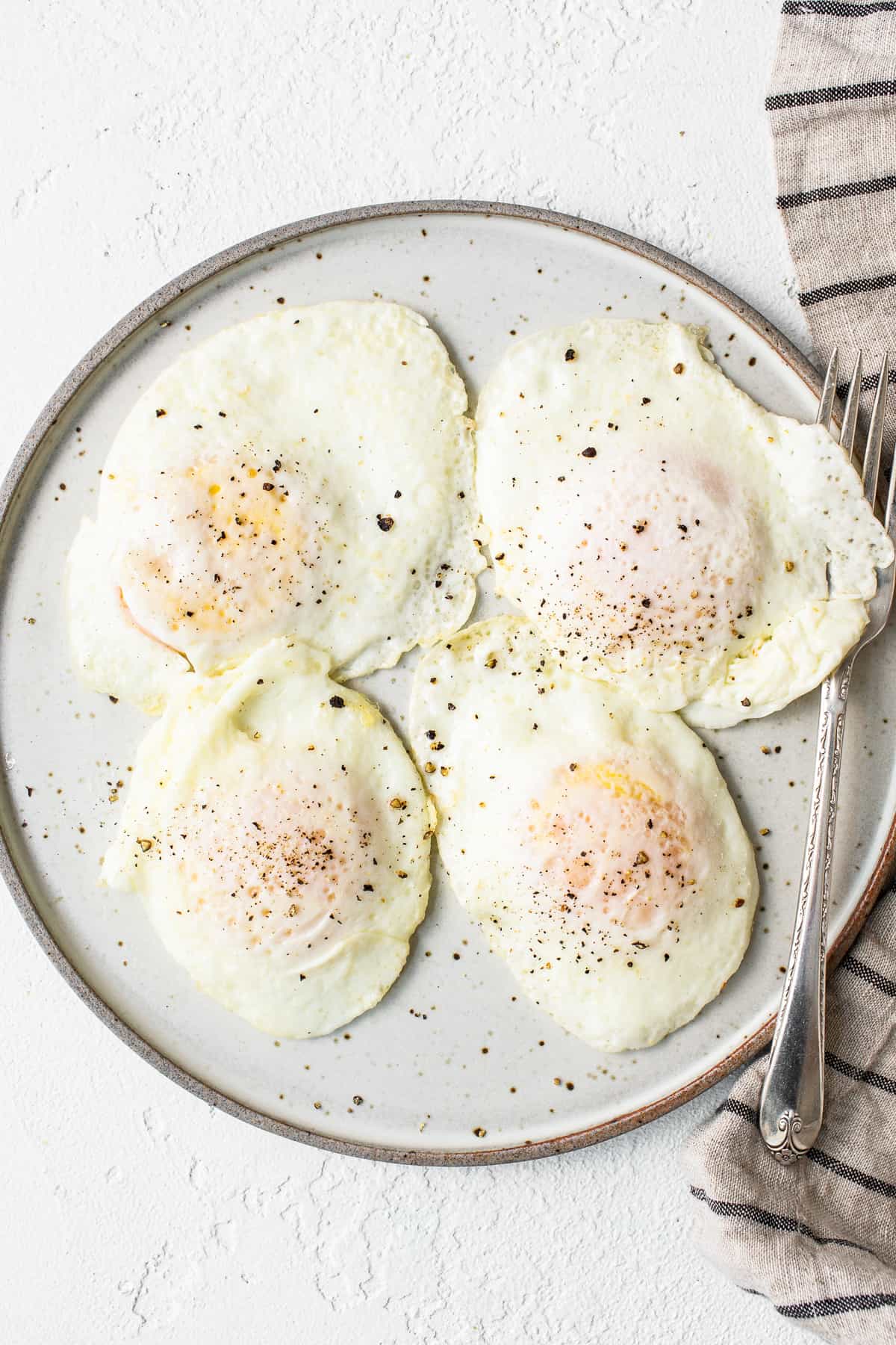 Over easy eggs on a plate with a fork.