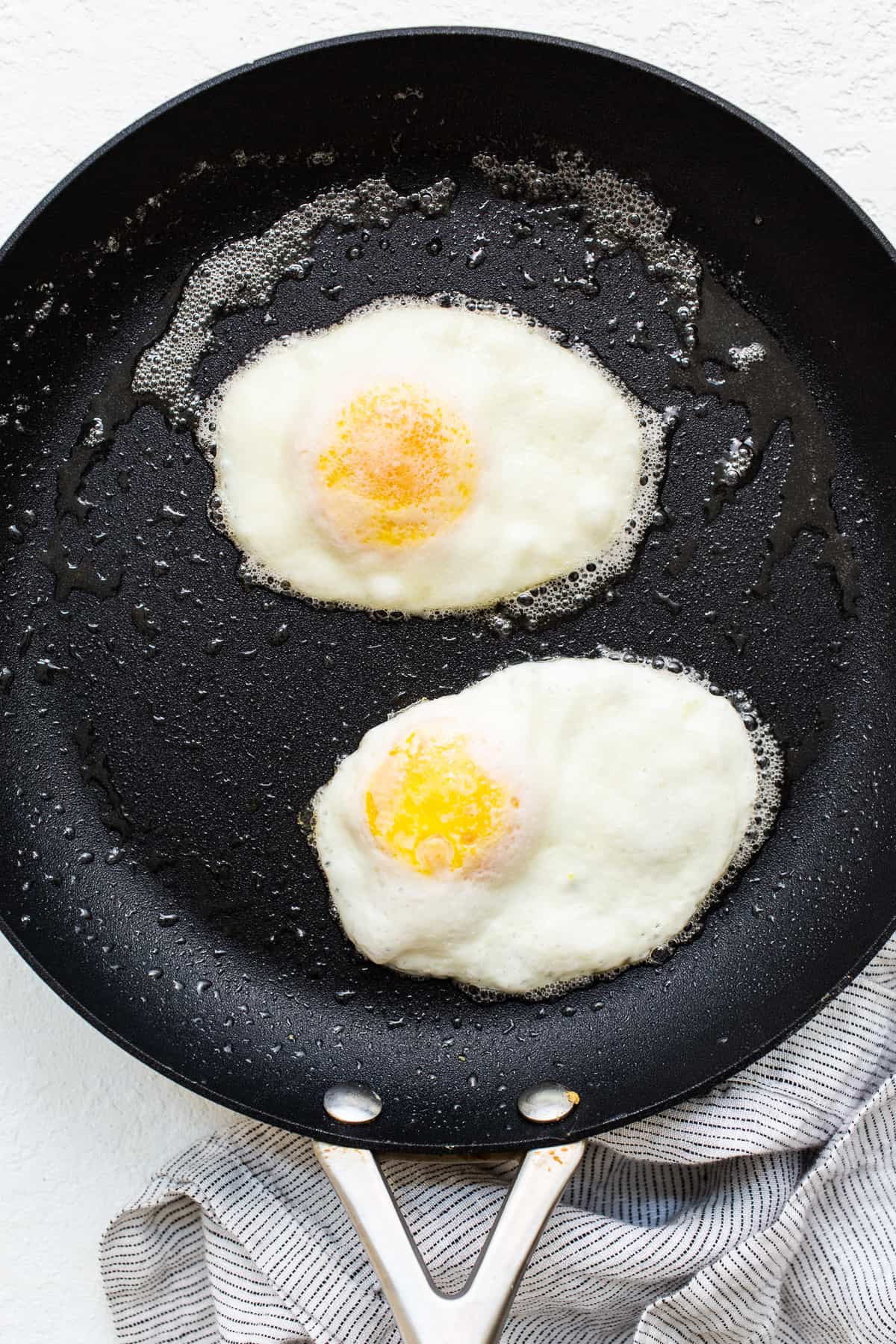 Over hard eggs cooking in a skillet with butter.