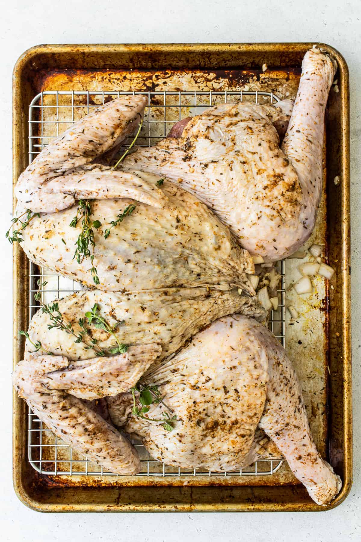 Spatchcocked turkey on a baking sheet with fresh herbs.