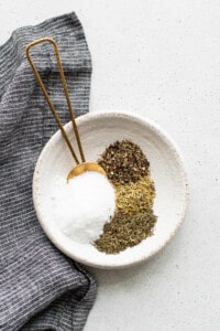 A white bowl with salt, pepper, and herbs.