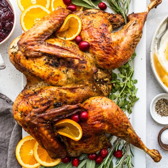 A roasted turkey on a platter with oranges and sage.