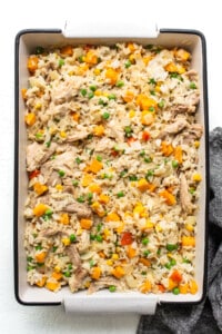 Chicken fried rice in a baking dish with carrots and peas.