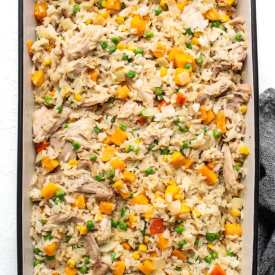 Chicken fried rice in a baking dish with carrots and peas.