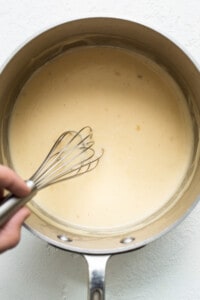 A person whisking a sauce in a pan.