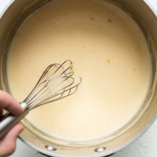 A person whisking a sauce in a pan.