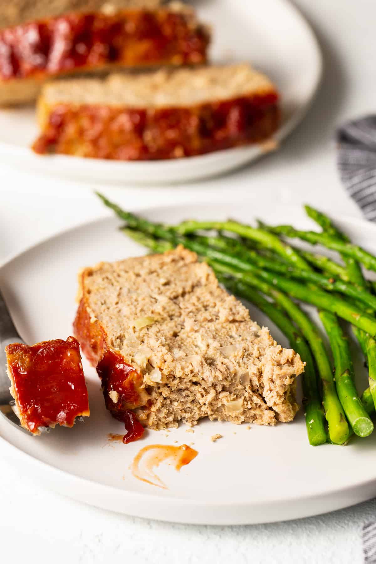 Slice of ground turkey meatloaf on a plate with asparagus.