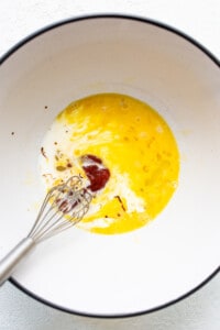 An egg in a bowl with a whisk.