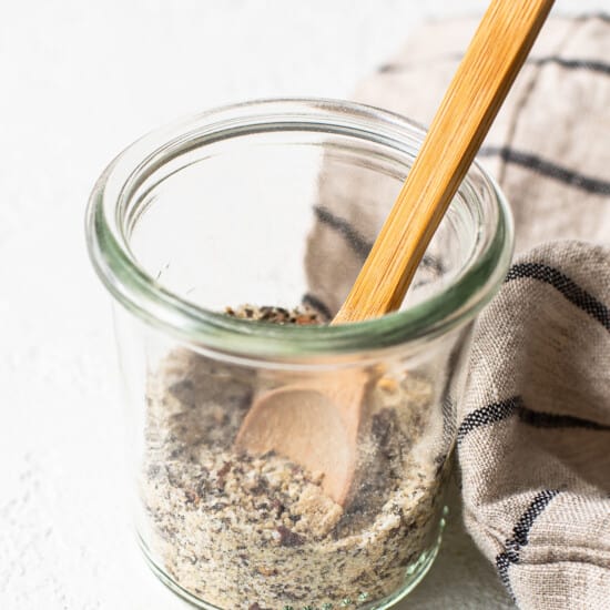 A glass jar with seeds and a wooden spoon.