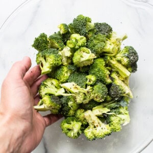 A person holding broccoli in a glass bowl.
