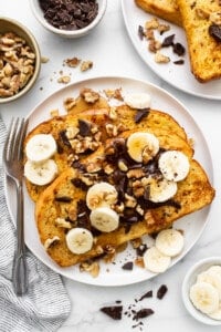 A plate of french toast with bananas, nuts and chocolate.